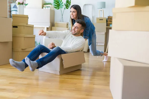 Young couple moving to a new home, having fun riding cardboard b — Stock Photo, Image