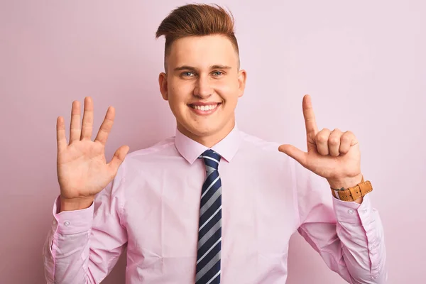 シャツとネクタイを着た若いハンサムなビジネスマンは 自信を持って幸せに微笑みながら 指番号7を示し 指で指を上げる孤立したピンクの背景の上に立って — ストック写真