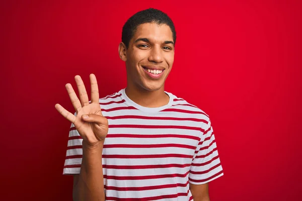 年轻英俊的阿拉伯男子穿着条纹T恤 披着孤立的红色背景 带着四号手指指尖 面带微笑 自信而快乐 — 图库照片