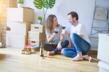 Orta yaş Senior romantik çift aşk yeni bir eve taşımak için mutlu gülümseyen bir bardak şarap içme kutluyor, etrafında kutuları ile daire katında oturan