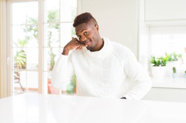 Yakışıklı afro-amerikan adam beyaz masada gülümseyerek telefonda konuşmak gibi el ve parmakları ile telefon jest yapıyor. İletişim kavramları.