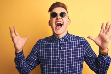 Sarı arka planda güneş gözlüğü takan genç ve yakışıklı bir adam sinirli bir şekilde bağırıyor ve bağırıyor. Saldırgan bir ifade ve kollar havada. Hayal kırıklığı konsepti.