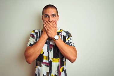 Beyaz arka plan üzerine yaz tişörtü giyen yakışıklı genç bir adam yanlışlıkla ağızlarını kapatarak şok geçirdi. Gizli konsept.