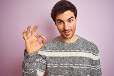 Genç yakışıklı adam parmakları, mükemmel sembolü ile ok işareti yapıyor izole pembe arka plan üzerinde duran rahat çizgili kazak giyiyor
