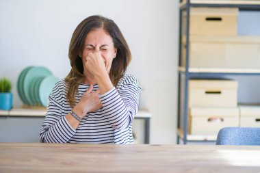 Evde masada oturan orta yaş yaşlı kadın, kokuşmuş ve bir koku, dayanılmaz bir koku, burun parmaklarıyla nefes tutuyor. Kötü kokular kavramı.