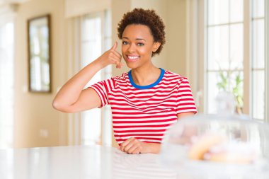 Genç güzel Afrikalı-Amerikalı kadın evde gülümseyen el ve parmak telefonda konuşmak ile telefon jest yapıyor. Kavramları iletişim.