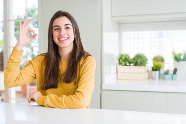 Sarı kazak giyen güzel genç kadın gülümseyerek olumlu el ve parmakları ile ok işareti yapıyor. Başarılı ifade.