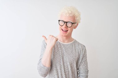 Genç albino sarışın adam çizgili t-shirt ve gözlük izole beyaz arka plan üzerinde mutlu yüz görünümlü gülümseyerek giyen ve başparmak ile yan işaret.