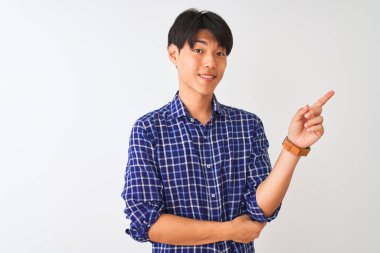 Genç Çinli adam yüzünde büyük bir gülümseme ile izole beyaz arka plan üzerinde duran rahat mavi gömlek giyen, kameraya bakarak yan el ve parmak ile işaret.