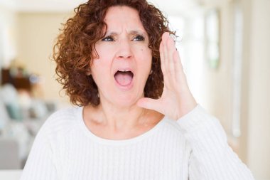 Güzel yaşlı kadın beyaz kazak giyen bağırarak ve ağızda el ile yan yüksek sesle bağırıyor. İletişim kavramı.