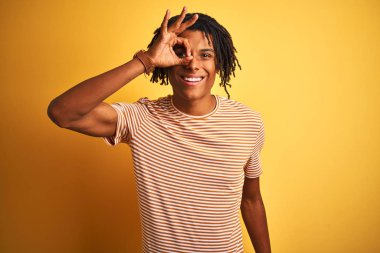 Çizgili t-shirt giyen dreadlocks giyen Afro adam izole sarı arka plan üzerinde duran el gülümseyerek ok jest yapıyor, mutlu yüz ile parmakları ile bakan göz.
