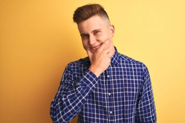 İzole edilmiş sarı arka plan üzerinde duran, kolları çapraz ve çenesi açık bir şekilde gülümseyen genç, yakışıklı bir adam. Olumlu düşünüyorum..