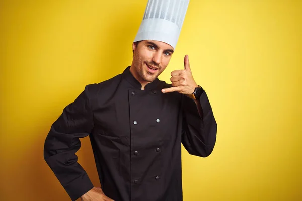 身穿制服 头戴帽子的年轻厨师站在孤立的黄色背景上 微笑着用手和手指做电话手势 就像在打电话一样 沟通概念 — 图库照片