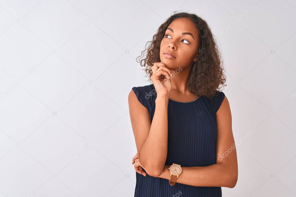 Young brazilian woman wearing blue dress standing over isolated white background with hand on chin thinking about question, pensive expression. Smiling with thoughtful face. Doubt concept.