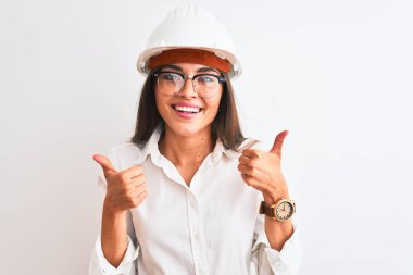 Kask ve gözlük takan genç, güzel bir mimar kadın izole edilmiş beyaz arka plan başarı tabelasına el hareketleriyle olumlu bir hareket yapıyor, gülümseyerek ve mutlu. Neşeli ifade ve kazanan jest.