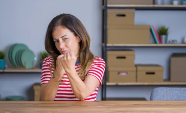 Evde masada oturan orta yaş yaşlı kadın yumruk savunma jesti ile mücadeleetmeye hazır, kızgın ve üzgün yüz, sorun korkuyor