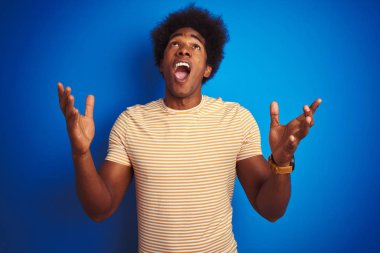 Afro saçlı Amerikalı adam izole mavi arka plan üzerinde çizgili sarı t-shirt giyen deli ve deli bağırarak ve agresif ifade ve kollar kaldırdı ile bağırıyor. Hayal kırıklığı kavramı.