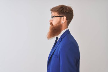 Genç kızıl İrlandalı işadamı yan bakarak izole beyaz arka plan üzerinde takım elbise ve gözlük giyen, kendine güvenen gülümseme ile doğal yüz ile profil poz dinlenmek.