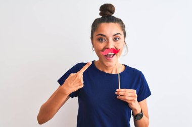 Genç, güzel bir kadın, izole edilmiş beyaz bir arka planda bel altı parti bıyığı tutuyor. El ve parmak göstererek çok mutlu.