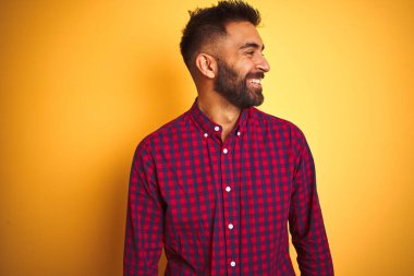 Izole sarı arka plan üzerinde duran rahat gömlek giyen genç hintli adam yüzünde gülümseme, doğal ifade ile yan bakıyor. Gülmekten emin.