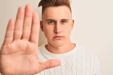 Yalnız beyaz arka plan üzerinde duran, ciddi ve kendinden emin bir ifadeyle dur işareti yapan, sıradan bir tişört giyen genç yakışıklı bir adam.
