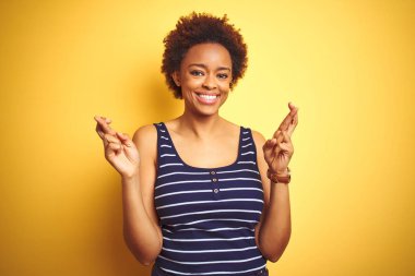Beauitul izole sarı arka plan gesturing parmak üzerinde yaz t-shirt giyen afrikalı amerikalı kadın umut ve gözleri kapalı gülümseyerek geçti. Şans ve batıl kavram.