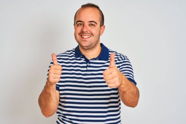 Sıradan çizgili polo giyen genç adam izole edilmiş beyaz arka planda duruyor. Elle olumlu jest yapmayı onaylıyor. Gülümsüyor ve başarı için seviniyor. Kazanan jest.