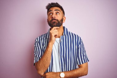 Genç yakışıklı hintli adam soru, dalgın ifade hakkında düşünme çene üzerinde el ile izole pembe arka plan üzerinde yaz çizgili gömlek giyiyor. Düşünceli bir yüzle gülümsüyor. Şüphe kavramı.