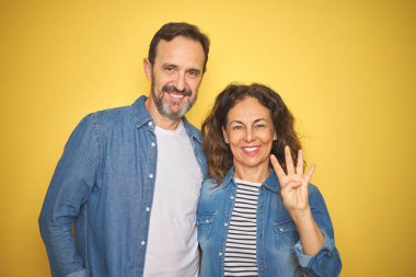 Güzel orta yaş çift birlikte izole sarı arka plan üzerinde denim gömlek giyen gösteren ve emin ve mutlu gülümserken parmakları ile dört numara işaret.