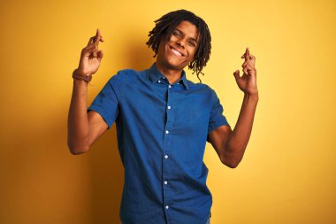 Izole sarı arka plan gesturing parmak üzerinde duran rahat kot gömlek giyen dreadlocks ile Afro adam umut ve gözleri kapalı gülümseyerek geçti. Şans ve batıl kavram.