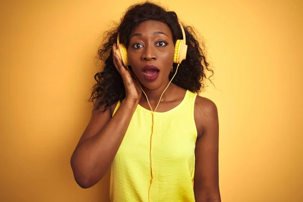 African american woman listening to music using headphones over isolated yellow background scared in shock with a surprise face, afraid and excited with fear expression