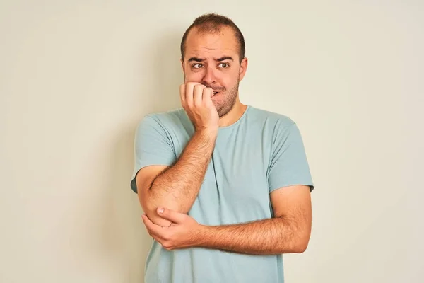 青いカジュアルなTシャツを着た若い男が 白い背景の上に立って 口の爪をかむ上で手で強調し 緊張している 不安の問題 — ストック写真