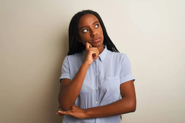 Young african american woman wearing striped shirt standing over isolated white background with hand on chin thinking about question, pensive expression. Smiling with thoughtful face. Doubt concept.
