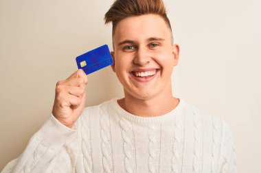 Genç ve yakışıklı bir adam kredi kartını soyutlanmış beyaz arka planda tutuyor. Mutlu bir yüzü var ve gülümsüyor. Dişlerini gösteren bir gülümsemeyle.