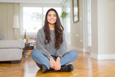 Genç güzel kadın yüzünde mutlu ve serin bir gülümseme ile evde yerde oturuyor. Şanslı kişi.