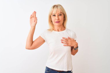 Orta yaş kadın göğüs ve açık avuç üzerinde el ile izole beyaz arka plan üzerinde duran rahat t-shirt giyen, bir sadakat yemini yapma