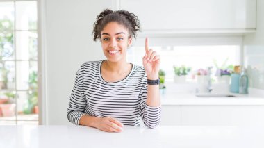 Afro saçlı güzel afro-amerikan kadın rahat çizgili kazak gösteren giyen ve kendinden emin ve mutlu gülümserken parmak sayısı bir ile işaret.