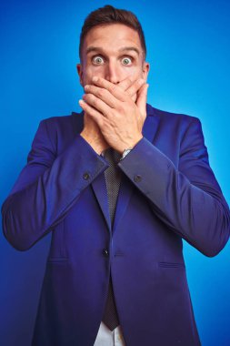 Mavi izole arka plan üzerinde genç yakışıklı iş adamı dikey açı resmi hata için elleri ile ağız kapsayan şok. Gizli kavram.