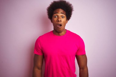 Afro saçlı, izole pembe arka plan üzerinde duran t-shirt giyen genç Amerikalı adam korkmuş ve sürpriz ifade ile şok, korku ve heyecanlı yüz.