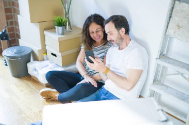 Orta yaş üst düzey romantik çift aşk etrafında kutuları ile daire katında oturan ve akıllı telefon yeni bir eve taşımak için mutlu gülümseyen kullanarak