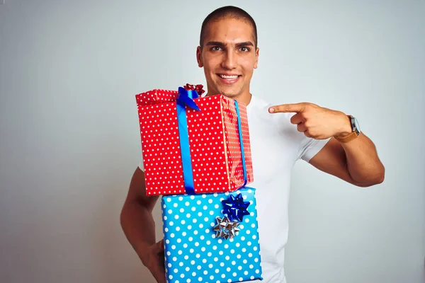 Young handsome man holding birthday gifts over white isolated background very happy pointing with hand and finger