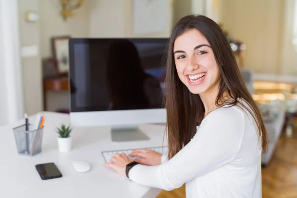 Mujer joven sonriendo trabajando con el ordenador y mostrando una s en blanco —  Fotos de Stock