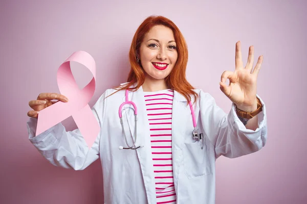 Junge Rothaarige Ärztin Hält Krebsband Über Rosa Isolierten Hintergrund Tun — Stockfoto