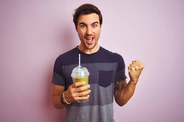 Young handsome man with tattoo drinking smoothie standing over isolated pink background screaming proud and celebrating victory and success very excited, cheering emotion