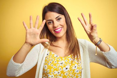 Sarı arka plan üzerinde duran ceketli genç ve güzel bir kadın 8 numaralı parmaklarıyla gülümseyerek kendinden emin ve mutlu görünüyor..