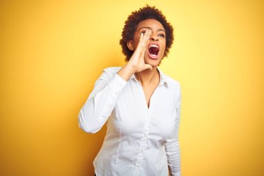 Izole sarı arka plan üzerinde Afrikalı Amerikalı iş kadını bağırarak ve ağızda el ile yan yüksek sesle bağırıyor. İletişim kavramı.
