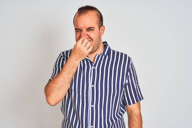 İzole edilmiş beyaz arka plan üzerinde duran mavi çizgili bir gömlek giyen genç adam pis ve iğrenç bir koku alıyor, dayanılmaz bir koku, parmakları burnunda nefesini tutuyor. Kötü koku konsepti.