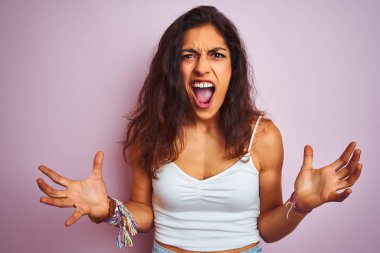Beyaz tişört giyen genç güzel kadın izole pembe arka plan üzerinde duran deli ve deli bağırarak ve agresif ifade ve kollar kaldırdı ile bağırıyor. Hayal kırıklığı kavramı.