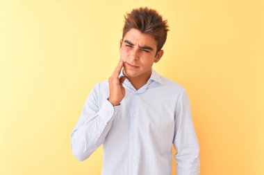 Genç yakışıklı iş adamı, diş ağrısı ya da diş ağrısı yüzünden izole edilmiş sarı arka planda zarif bir gömlek giyer ve ağıza acı dolu bir ifadeyle dokunur. Dişçi konsepti.
