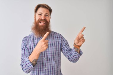 Genç kızıl İrlandalı adam izole beyaz arka plan üzerinde gülümseyerek ayakta rahat gömlek giyen ve yan iki el ve parmakları ile işaret kamera bakarak.